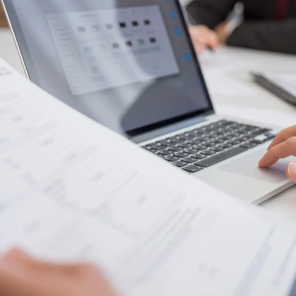A close-up of a laptop with documents and papers on the desk